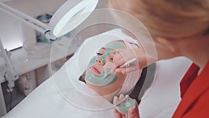 young woman in cosmetologist appointment, lying and relaxing, aesthetician applying clay mask