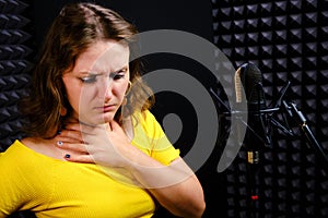 Young woman coughs next to the microphone and holds her throat. Trouble with the voice of the singer in the performance of the