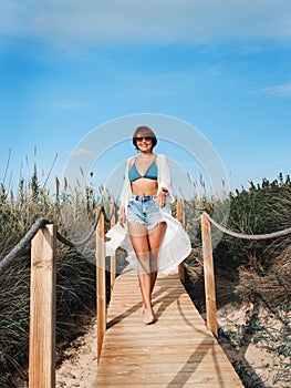 Young woman in cover up and jeans shorts walking between dunes photo