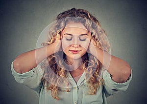 Young woman covering ears avoiding noise on gray background