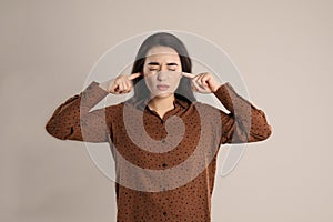 Young woman covering ears with fingers on beige background