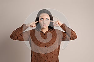 Young woman covering ears with fingers on beige background