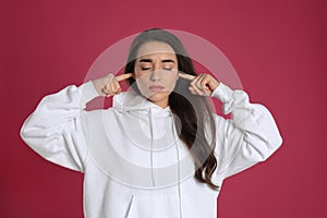 Young woman covering ears with fingers on pink background