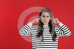 Young woman covering ears with fingers on red background