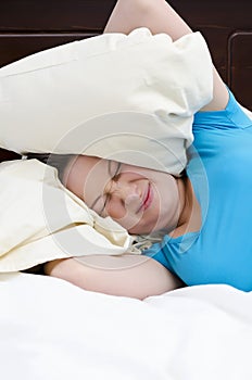 Young woman covering ears with pillow