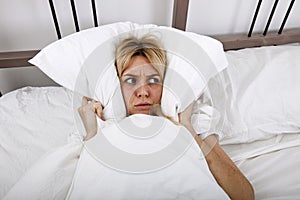 Young woman covering ears with pillow in bed