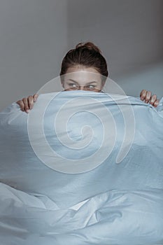 Young woman covering face with bedcover in bed