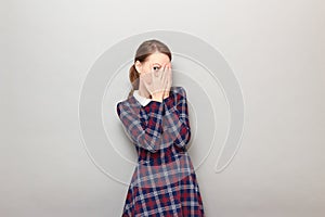 Young woman is covering face and looking through fingers at something