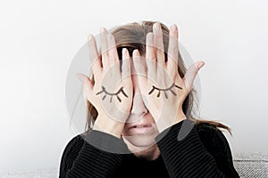 Young woman is covering her eyes with her palms. Eyes painted on her hand.