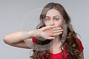 Young woman covering mouth with hand, looking serious, promises to keep secret. Silence and secret concept