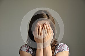 A young woman covers her face with hands