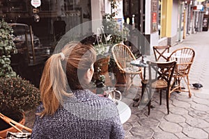 Young woman in a cozy gray-blue vest spends time in street cafe