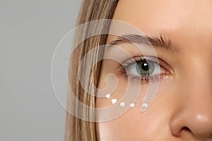 Young woman with cream around eye on light grey background, closeup. Space for text