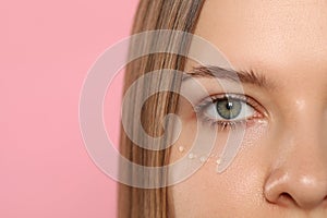 Young woman with cream around eye on pink background, closeup. Space for text