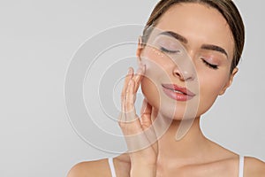 Young woman with cream around eye on white background, closeup. Space for text