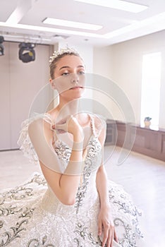 A young woman in a cream-colored dress wearing a crown is putting on her makeup in front of the mirror. The concept of beauty