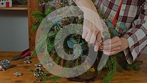 Young woman creates Christmas flower arrangement to decorate festive table.