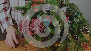 Young woman creates Christmas flower arrangement to decorate festive table.