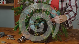 Young woman creates Christmas flower arrangement to decorate festive table.