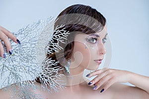 Young woman in creative silver artistic make-up.Fairy Ice Queen elegant pose, silver and white branches,magic winter