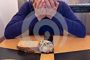 Young woman cries and buries her head and face while sitting at a kitchen table with a scone and toast. Concept for dieting and