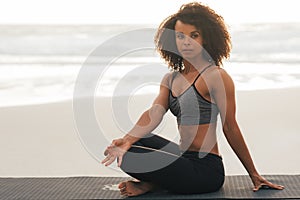 Young woman with crossed legs doing meditation practice at sunset. Healthy female sitting on mat doing yoga exercises