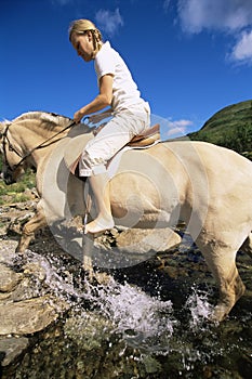 Young woman crossing a river by horse