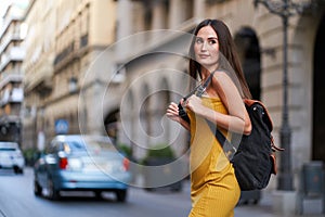 young woman crossing a street with traffic with her backpack on her back