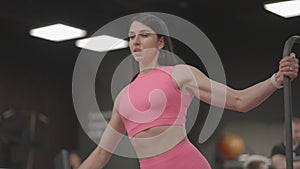 A young woman in a crossover raises her shoulder arms in a pink suit. Exercises for training the arms and shoulders