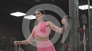 A young woman in a crossover raises her shoulder arms in a pink suit. Exercises for training the arms and shoulders