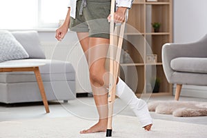 Young woman with crutch and broken leg in cast at home