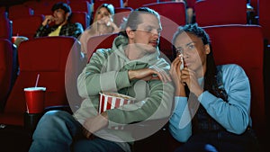 Young woman crying, looking emotional while watching movie together with her boyfriend, sitting in cinema auditorium