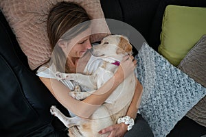 Young woman cuddling with her cute white dog sleeping in her lap