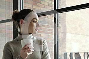 Young woman with a cup of coffee looking in the window