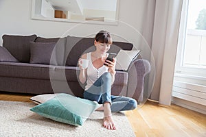 Young woman with a cup of coffee sits on the floor near the sofa