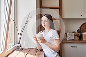 Young woman with cup of coffee or tea at window in coffee shop. Good morning concept. Cozy breakfast. Girl in cafe