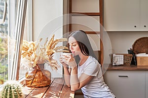 Young woman with cup of coffee or tea at window in coffee shop. Good morning concept. Cozy breakfast. Girl in cafe