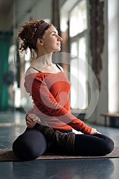 Young woman with curly hair doing bharadvajasana or seated spinal twist asana