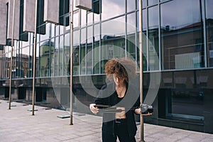 Young woman with curly hair is examining camera while standing outside the moderne marble building