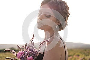 Young woman with curly hair posing near roses in a garden. The concept of perfume advertising