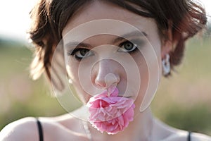 Young woman with curly hair posing near roses in a garden. The concept of perfume advertising