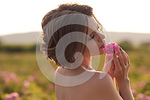 Young woman with curly hair posing near roses in a garden. The concept of perfume advertising