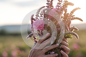 Young woman with curly hair posing near roses in a garden. The concept of perfume advertising