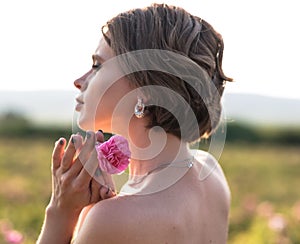 Young woman with curly hair posing near roses in a garden. The concept of perfume advertising