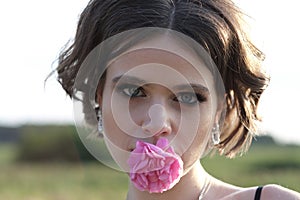 young woman with curly hair posing near roses in a garden. The concept of perfume advertising