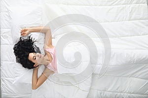 Young woman with curly hair sleeping in white bed top view
