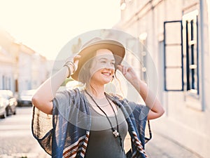 Young woman with curly hair walking on city street at sunset wearing hat and coat, enjoying happy moment on european street