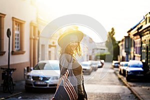 Young woman with curly hair walking on city street at sunset wearing hat and coat, enjoying happy moment on european street