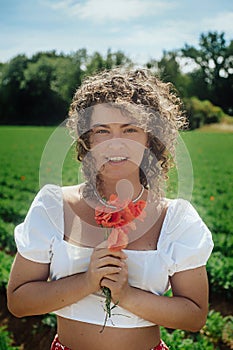 Young woman with curly hair in a white dress with a bouquet of flowers