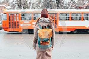 Young woman curly red head girl traveller with backpack in front of tram at the city street